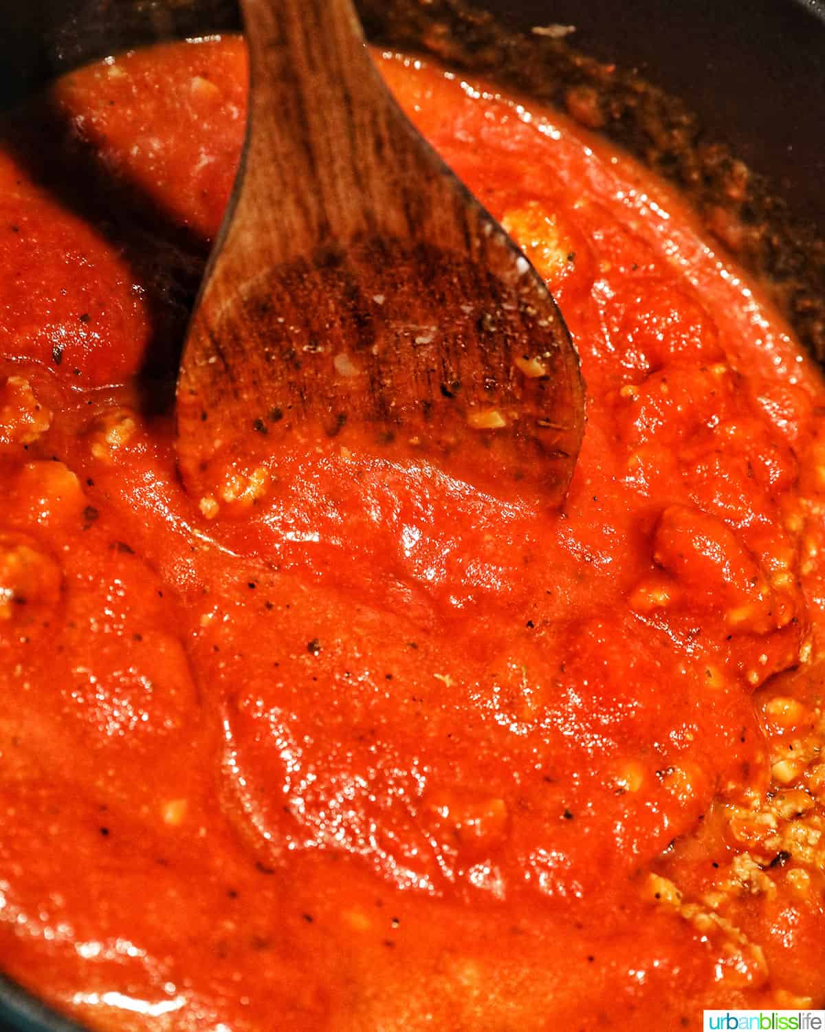 wooden spoon stirring marinara sauce in a dutch oven.