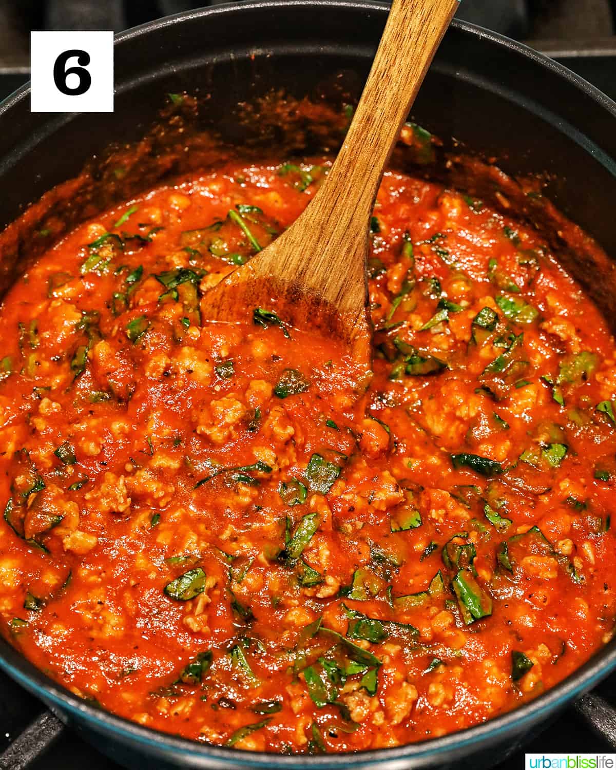 wooden spoon stirring ground turkey marinara sauce in a dutch oven.