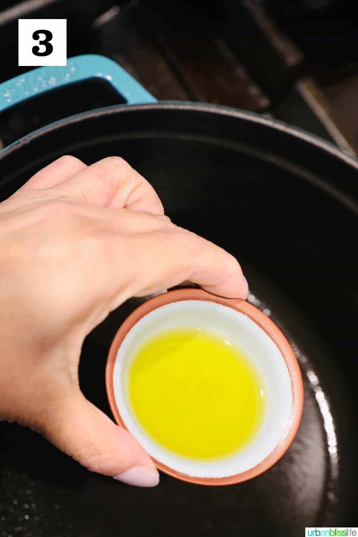 hand pouring a pinch bowl full of olive oil into a dutch oven.