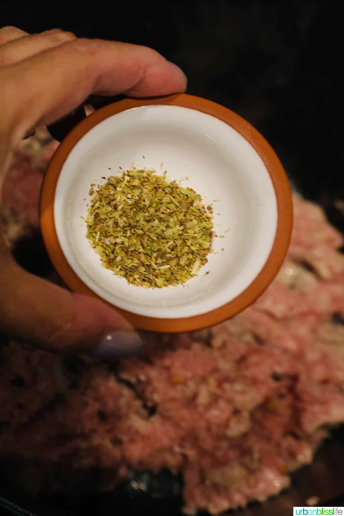 hand adding a pinch bowl of basil to the pot.