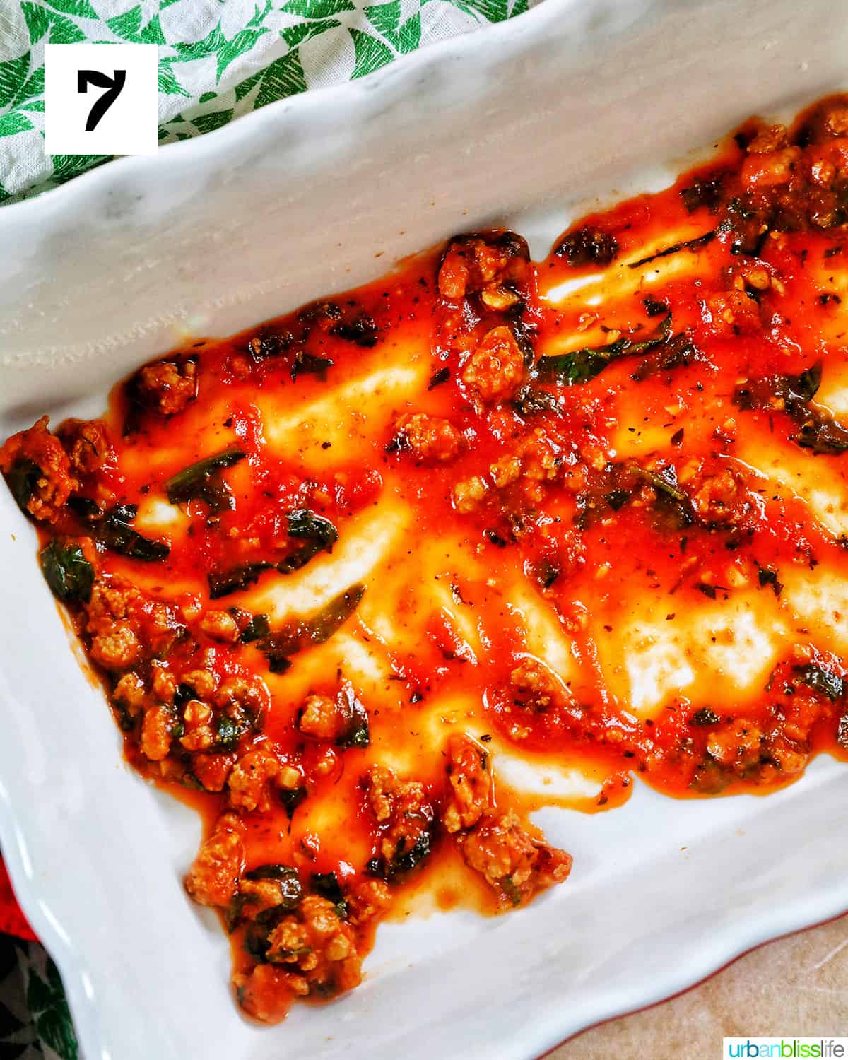 white baking dish with light pasta sauce smeared in a thin layer across the bottom.