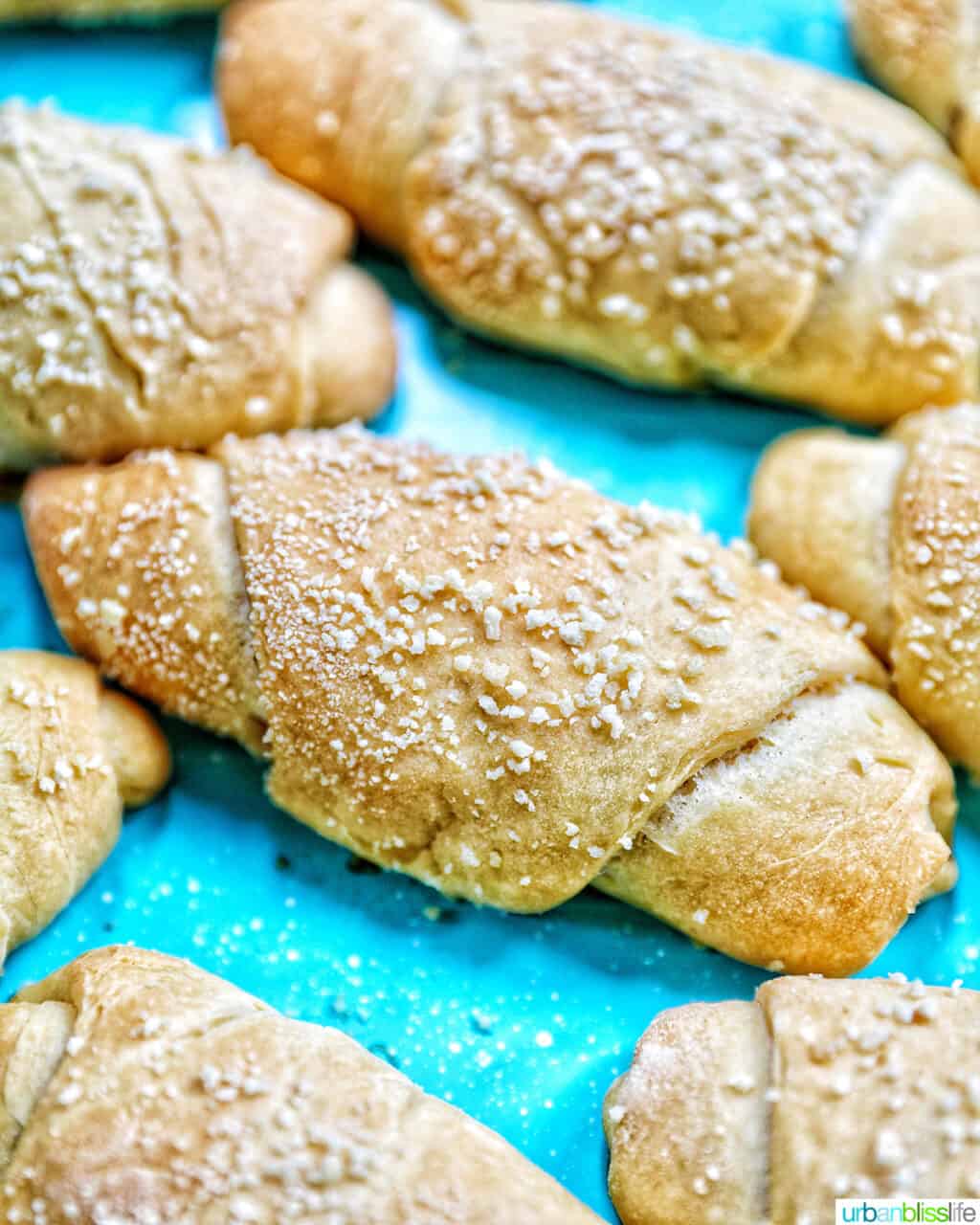 several freshly baked Filipino Spanish bread rolls with breadcrumbs on a bright blue background.