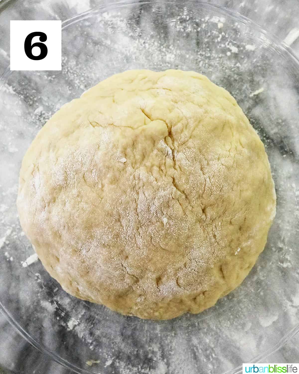 formed dough ball in a clear glass bowl on a marble countertop.