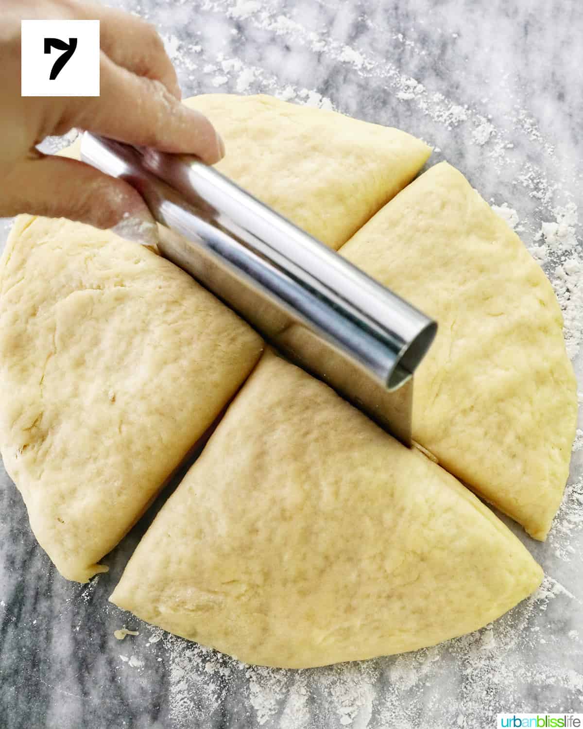 hand using a pastry bench to quarter a dough ball for spanish bread on a marble countertop.