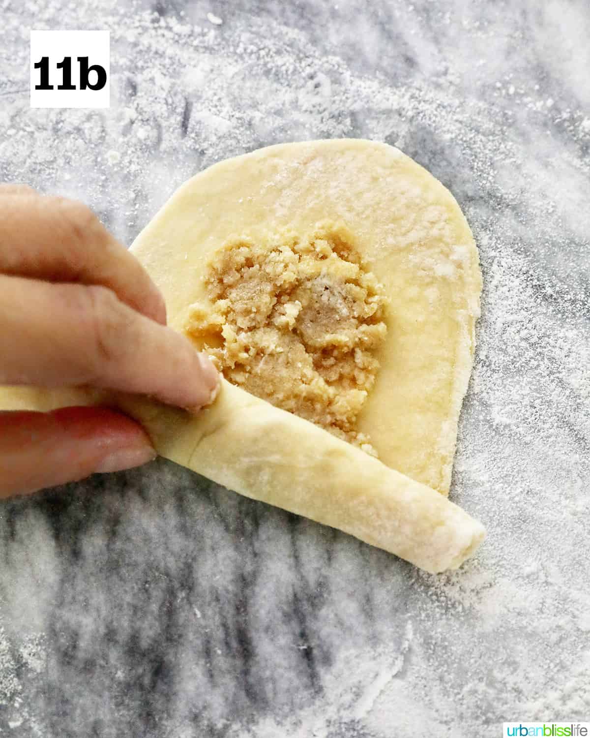 hand rolling up a filled spanish bread dough on marble countertop.