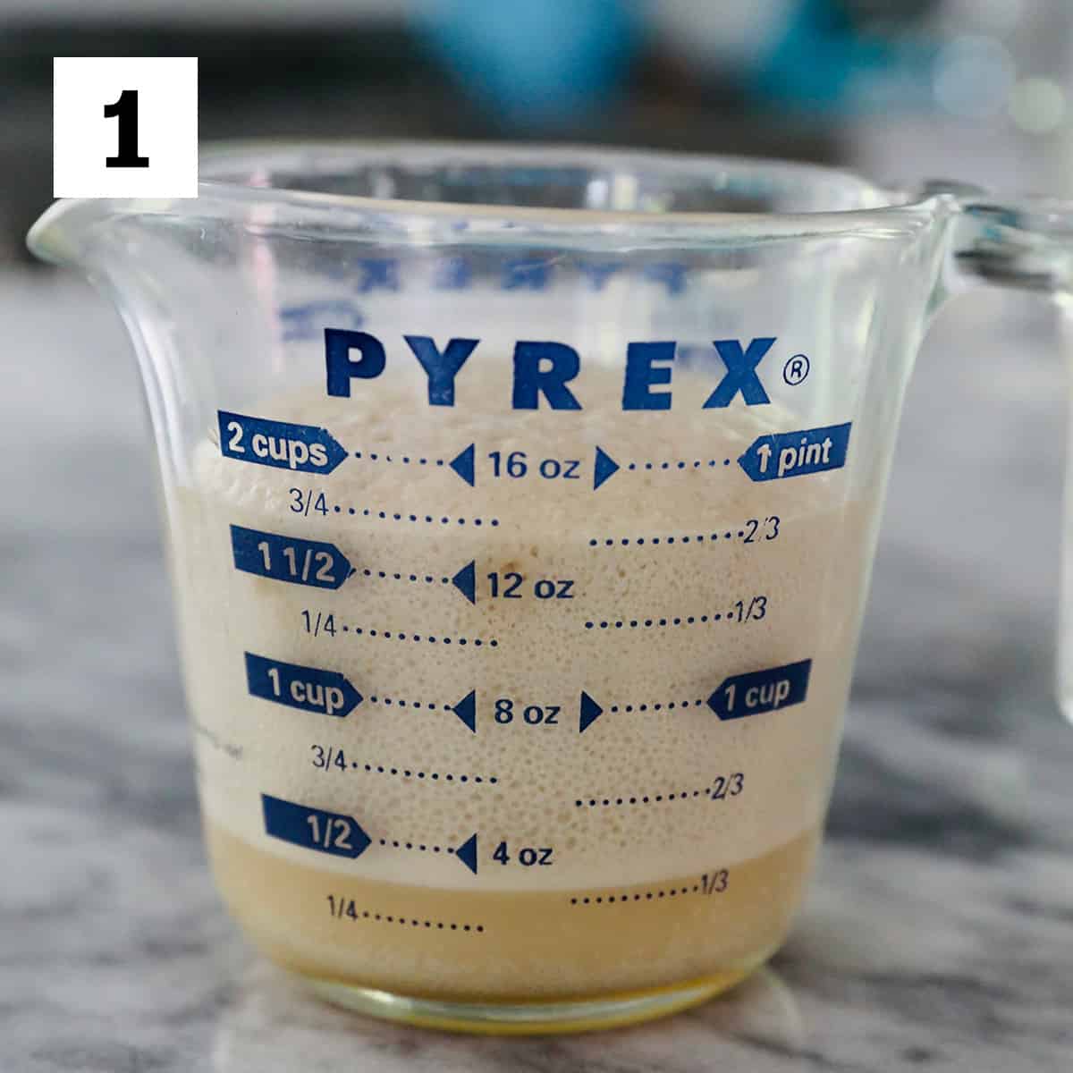 yeast activated in a Pyrex glass measuring cup on marble countertop.