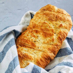 loaf of french bread in a basket lined with blue and white striped towel.