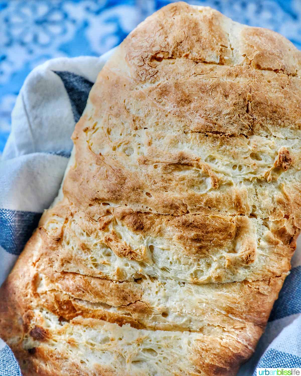 homemade French bread loaf in a basket with blue and white striped cloth on a tiled table.