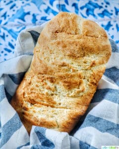homemade French bread loaf in a basket with blue and white striped cloth on a tiled table.