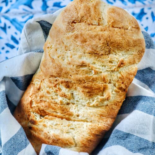 homemade French bread loaf in a basket with blue and white striped cloth on a tiled table.
