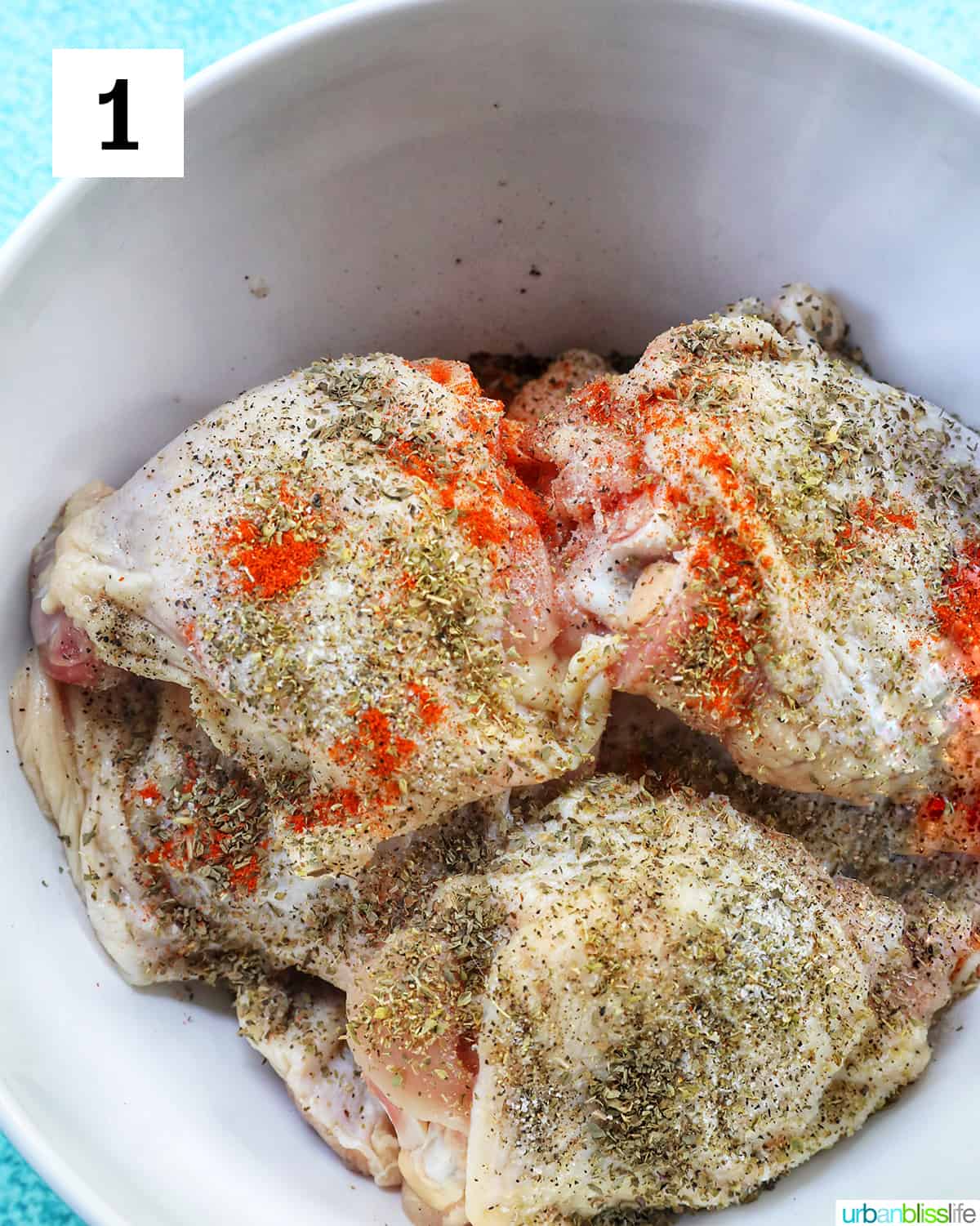 raw chicken thighs in a white bowl with seasoning.