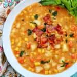white bowl filled with potato corn chowder, bacon, carrots, and side of parsley leaves.
