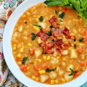 white bowl filled with potato corn chowder, bacon, carrots, and side of parsley leaves.