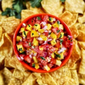 Mango pico de gallo in orange bowl surrounded by tortilla chips.