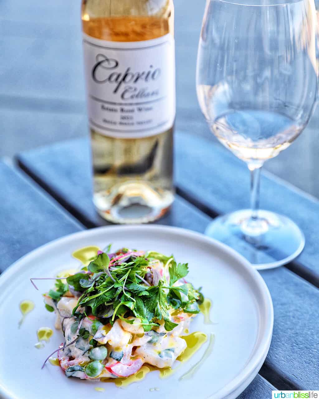 bottle of rosรฉ wine, rosรฉ wine in a glass, and a white plate topped with potato salad and microgreens.
