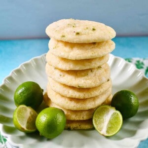 stack of key lime cookies on a plate next to several key limes.