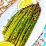 grilled asparagus with lemon wedges on a white plate and colorful napkin.