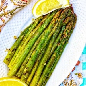 grilled asparagus with lemon wedges on a white plate and colorful napkin.