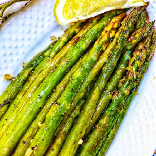 white serving plate with grilled asparagus, garlic, and lemon wedge.