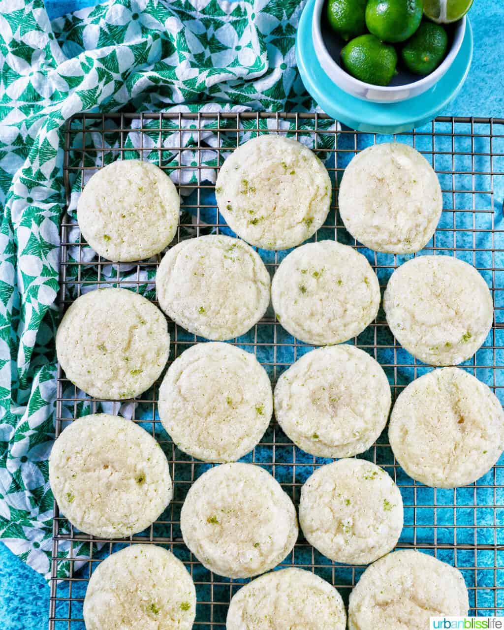 several key lime cookies laying on a baking rack with a bowl of key limes above.