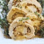 sliced stuffed pork loin on a white platter with herbs on the side and top.