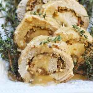 sliced stuffed pork loin on a white platter with herbs on the side and top.