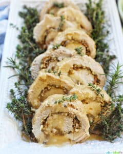 sliced stuffed pork loin on a white plate with a bed of herbs.