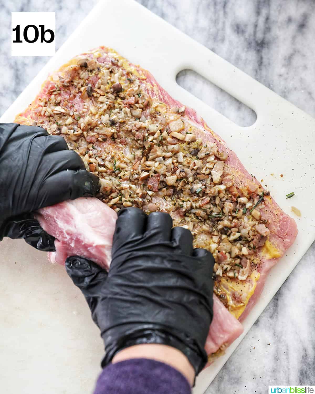 gloved hands rolling up the stuffed pork loin on a white cutting board.