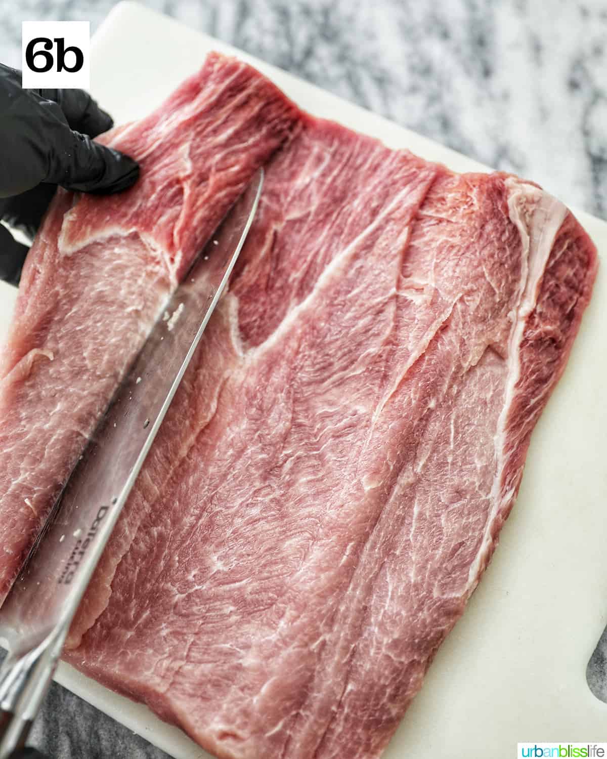 gloved hands slicing into the pork loin with a knife on a white cutting board.