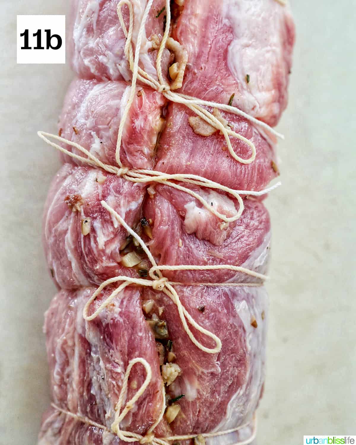 raw stuffed and rolled pork loin wrapped in kitchen twine on a white cutting board.
