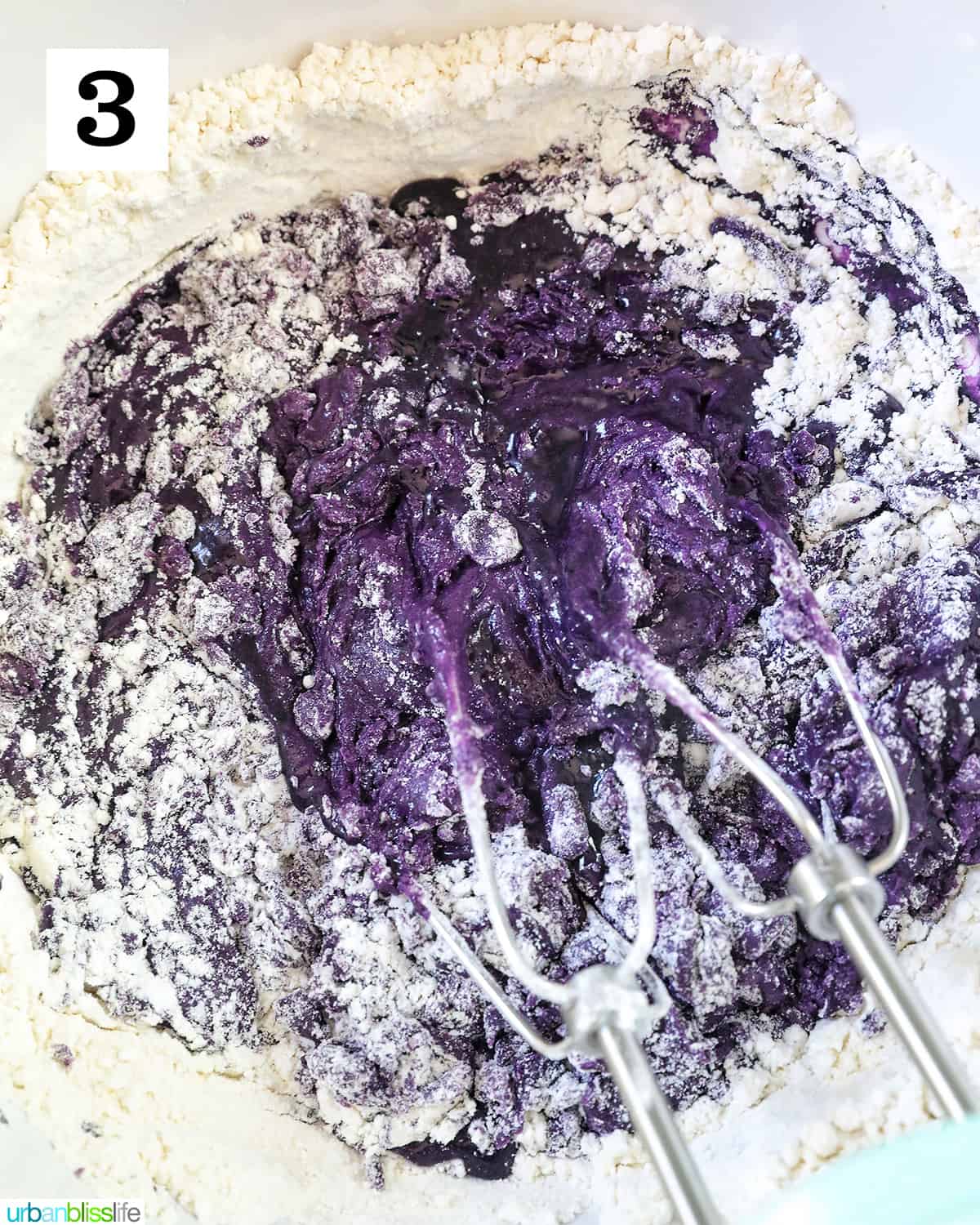 whisk in a white bowl with ube batter and flour dry ingredients.