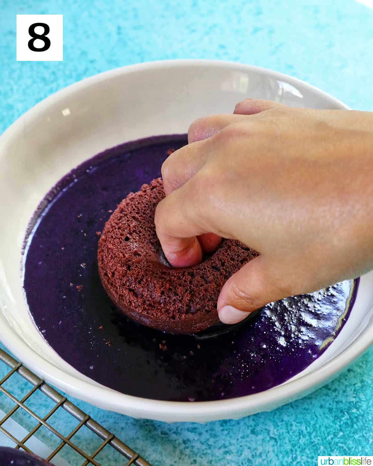 hand dipping a purple ube donut into a bowl of ube glaze.