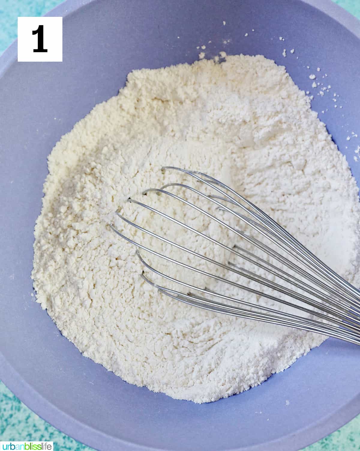 purple bowl with whisk in white dry ingredients.