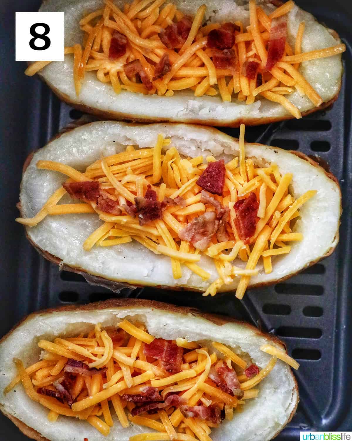 three potato skins topped with cheddar cheese and bacon in an air fryer basket.