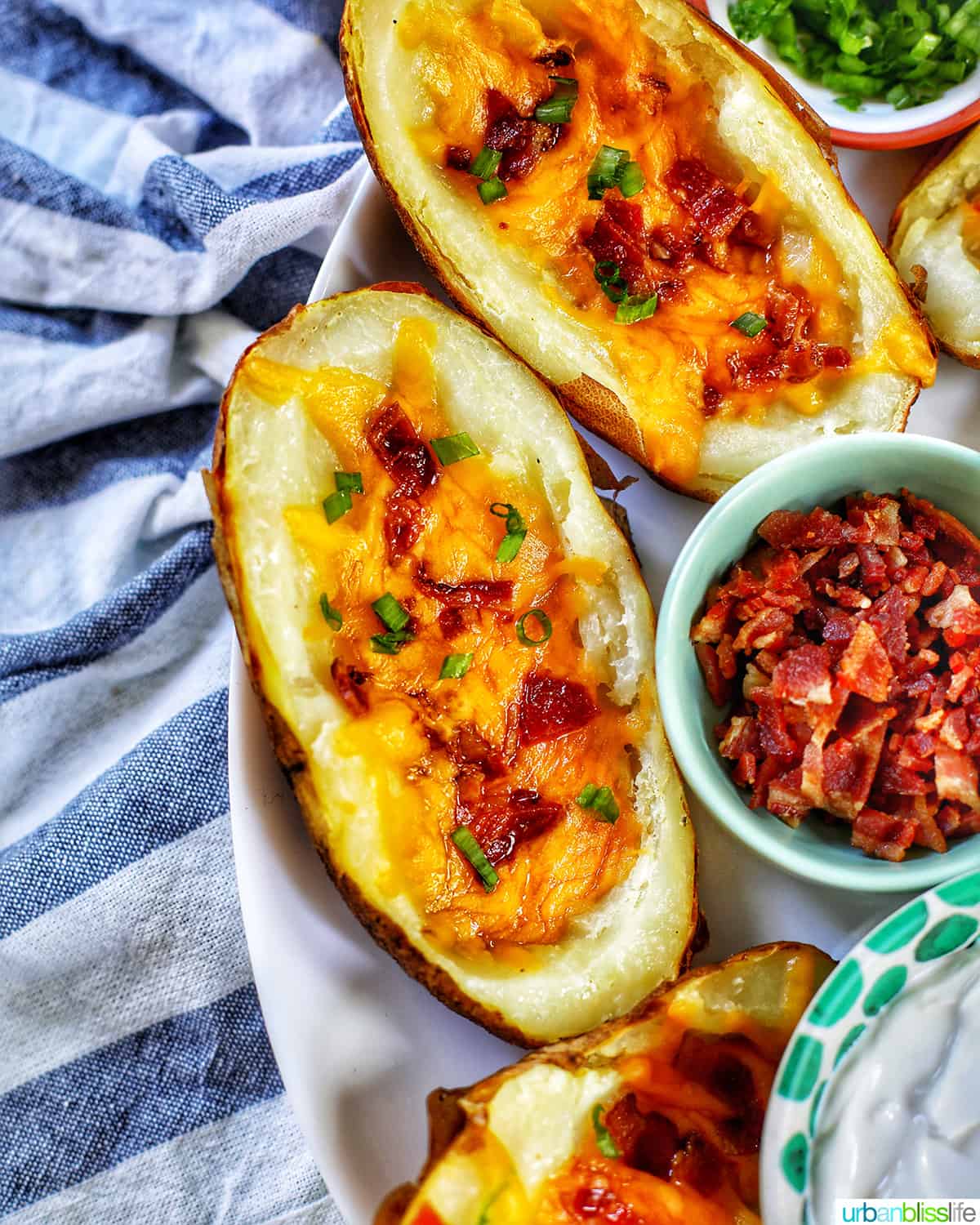 several air fryer potato skins with sides of green onions, bacon, and sour cream.