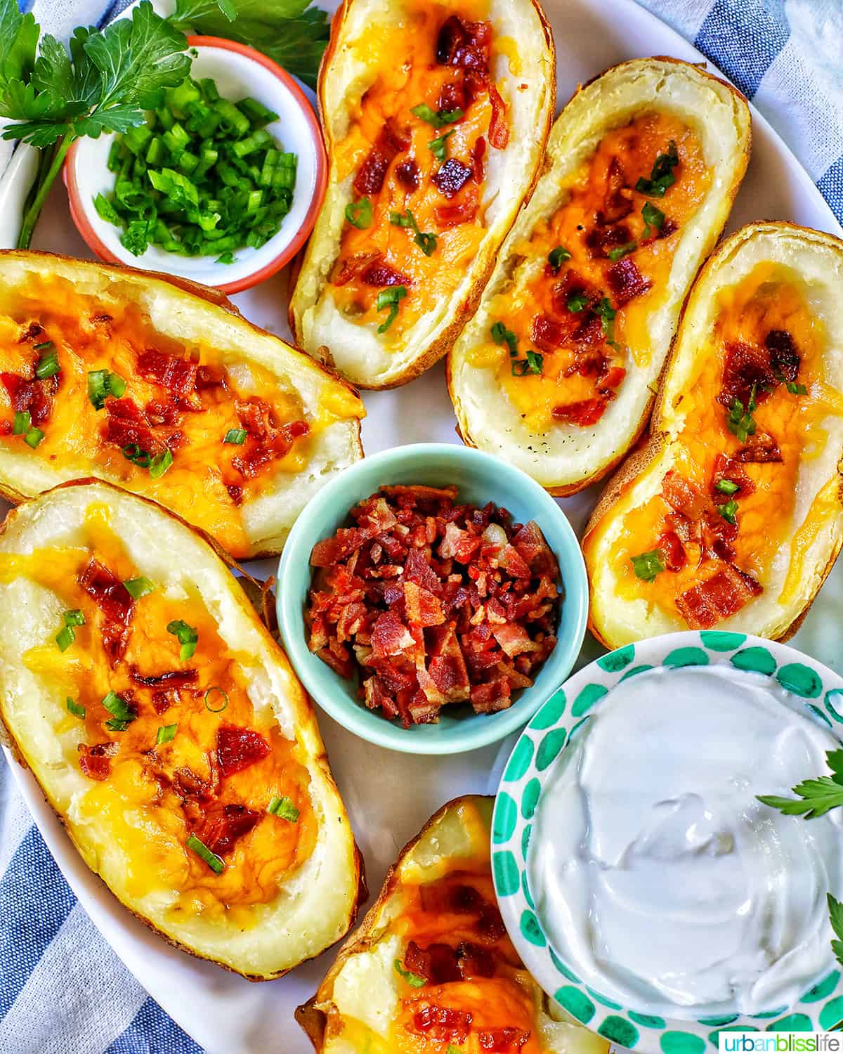 several air fryer potato skins with sides of green onions, bacon, and sour cream.