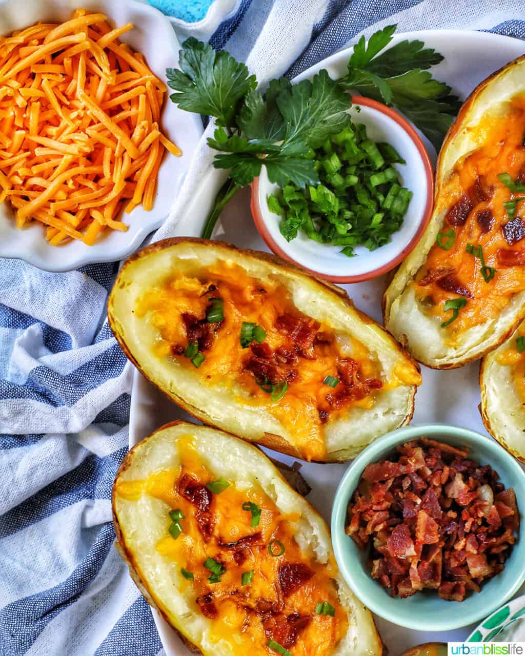 air fryer potato skins with sides of shredded cheddar cheese, green onions, bacon, on a white and blue napkin.