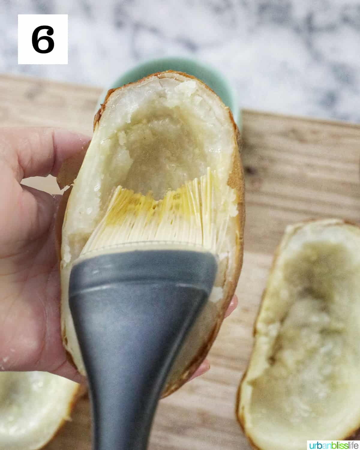 a pastry brush brushing a hollowed out potato half with olive oil.