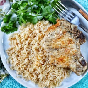 Instant Pot Pork Chops and Rice on a white plate with side of greens and fork and knife.