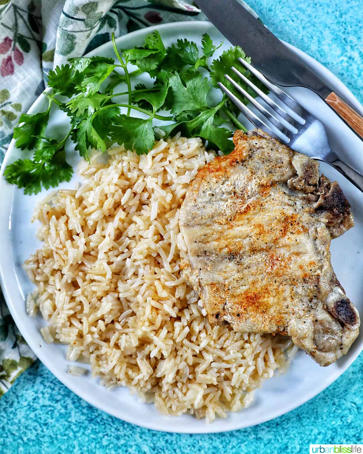 Instant Pot Pork Chops and Rice on a white plate with side of greens and fork and knife.