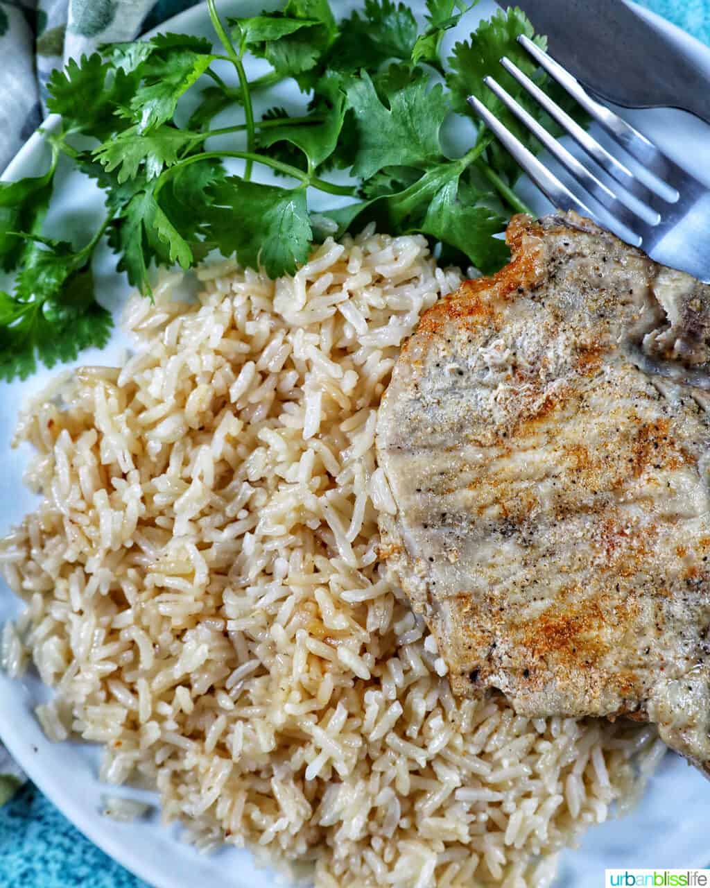 Instant Pot Pork Chops and Rice on a white plate with side of greens and fork and knife.