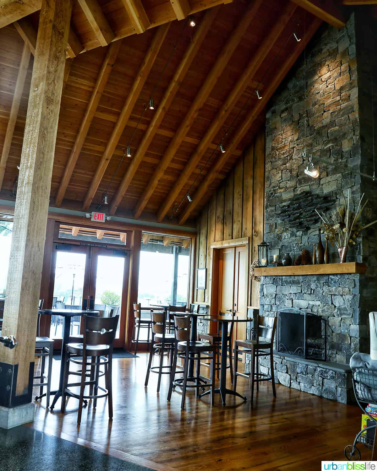 high top tables and chairs, a stone fireplace, and high wood-beam ceilings in the Kriselle Cellars tasting room.