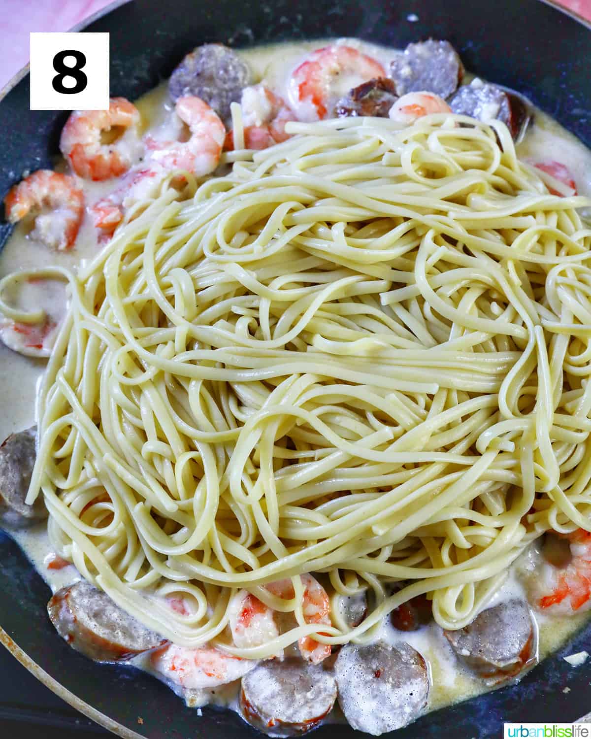 lots of linguine pasta added to a skillet of shrimp and sausage.