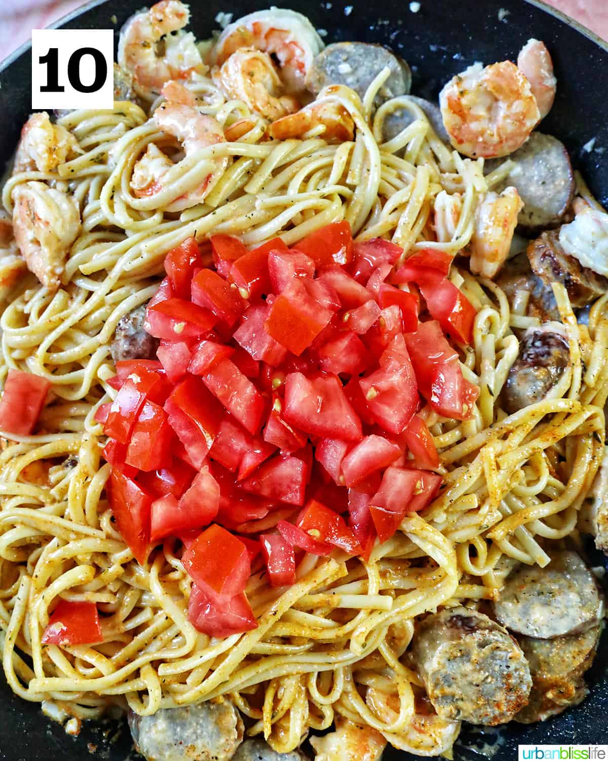 tomatoes added to shrimp and sausage pasta in a skillet.
