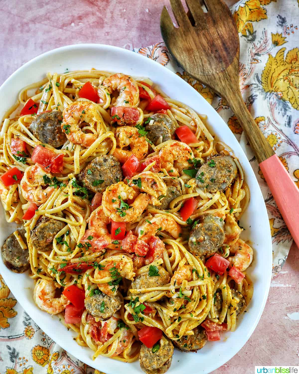 large serving platter of shrimp and sausage pasta with wooden spoon.