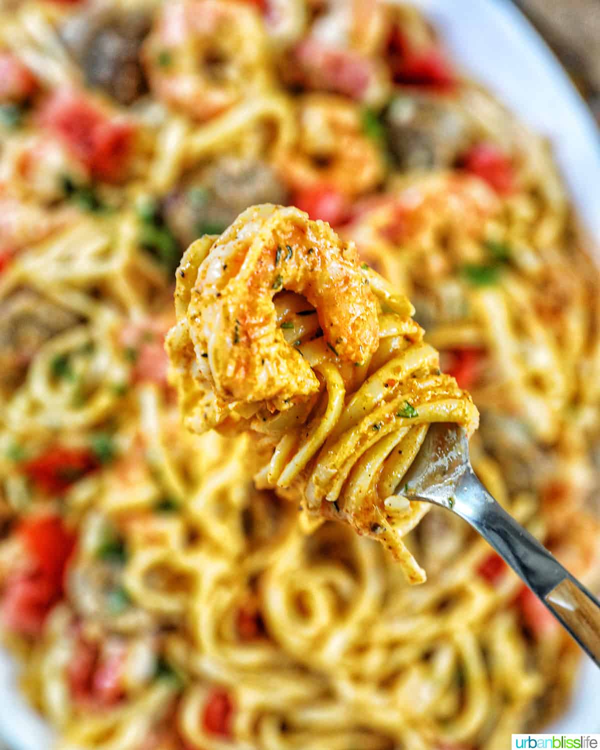 fork full of twirled pasta with a large bowl of shrimp and sausage pasta in the background.