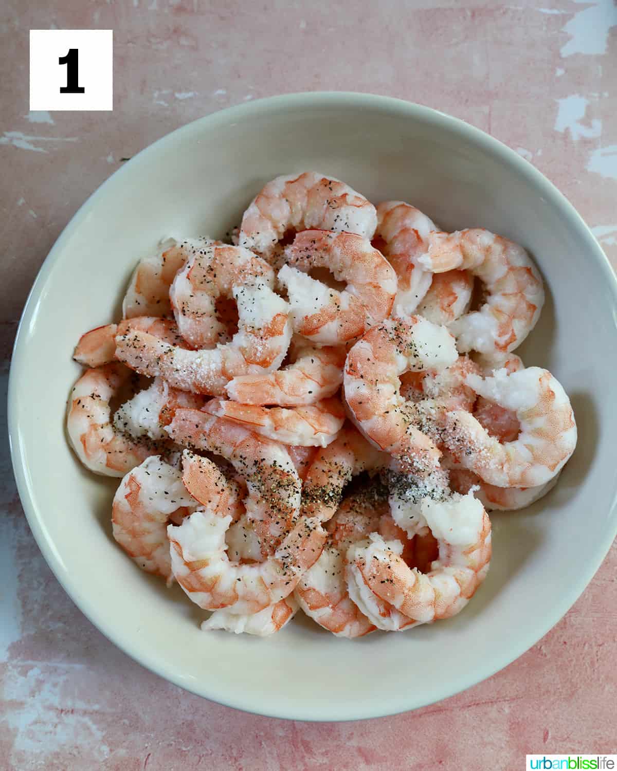 bowl full of raw shrimp for shrimp and sausage pasta on a peach colored table.