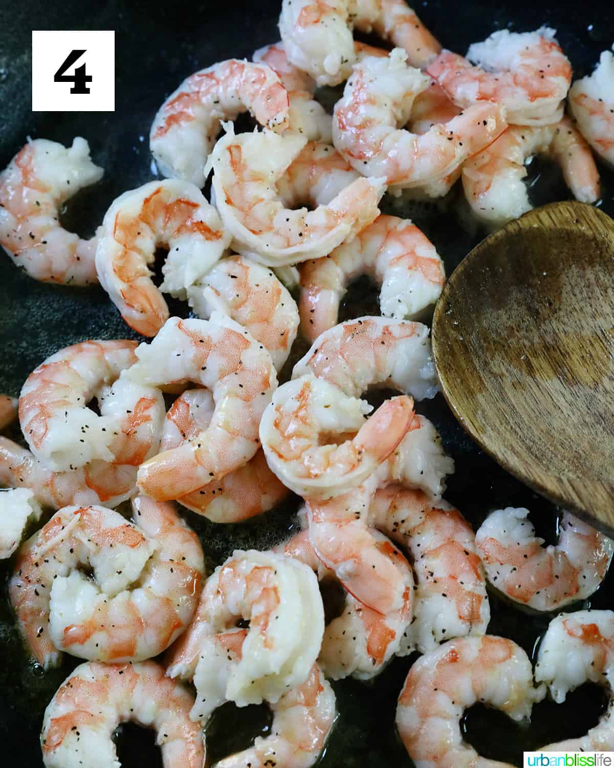 lots of shrimp added to the skillet with a wooden spoon.