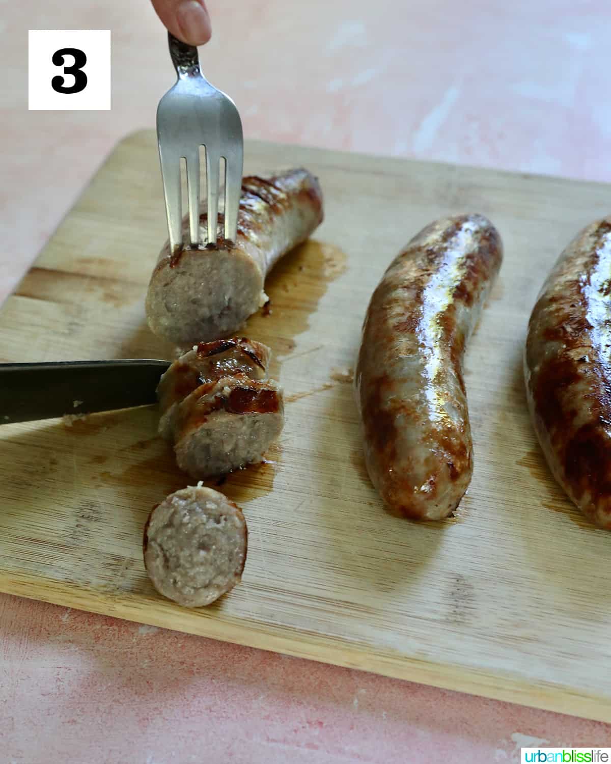 a fork and knife slicing into a sausage with two other sausages all on a cutting board.