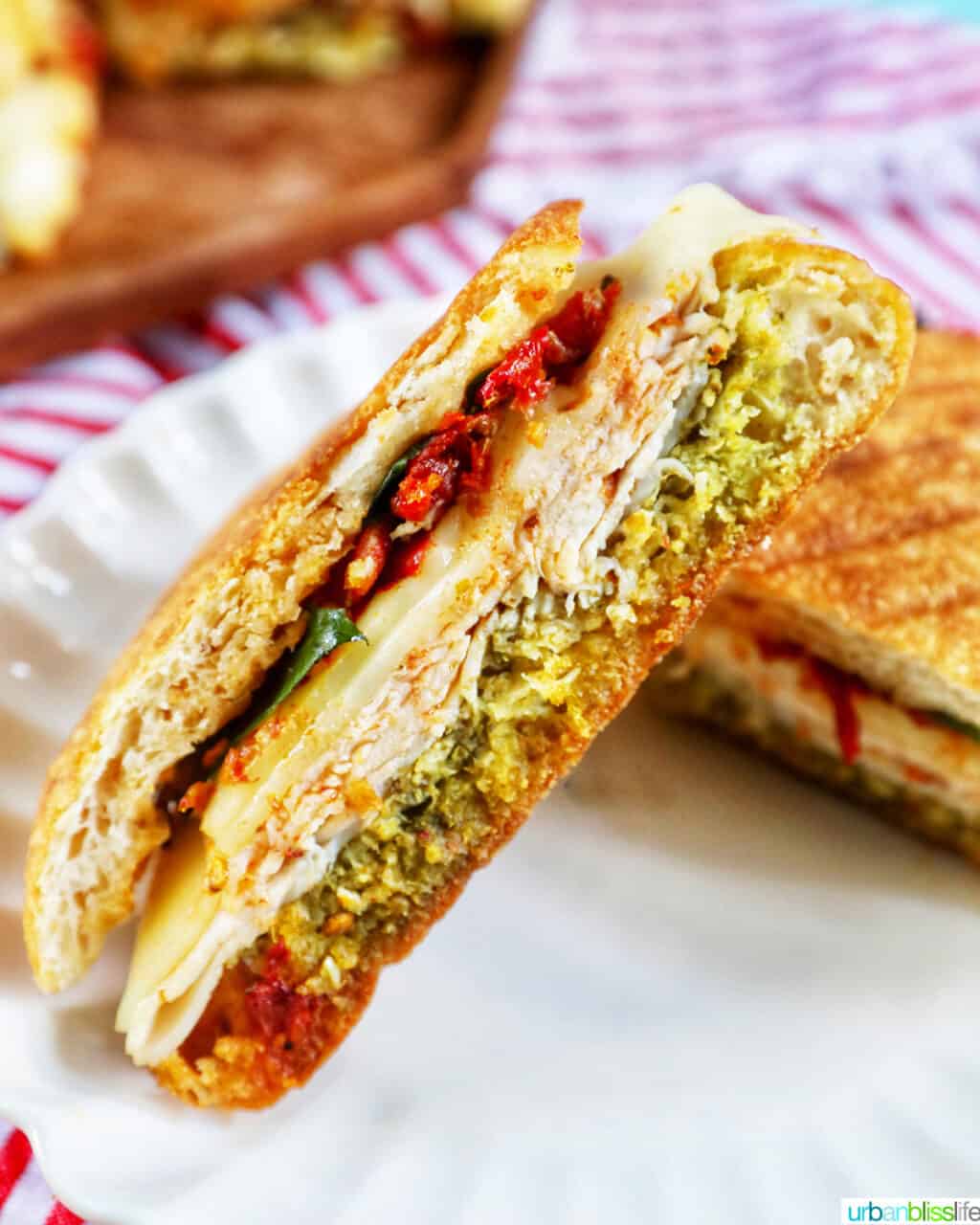 turkey pesto sandwich cut in half propped up on the other half of the sandwich on a white plate.
